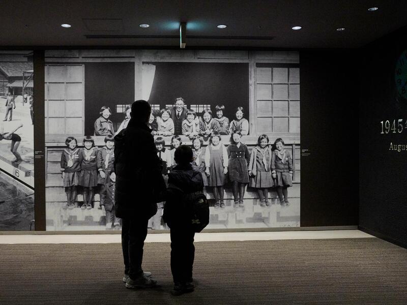 女学生の並んだモノクロ写真を見る親子の写真