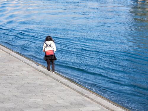 水辺を歩く女性の後ろ姿の写真