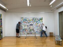 壁に作品を設置する栗原さんと助手さん
